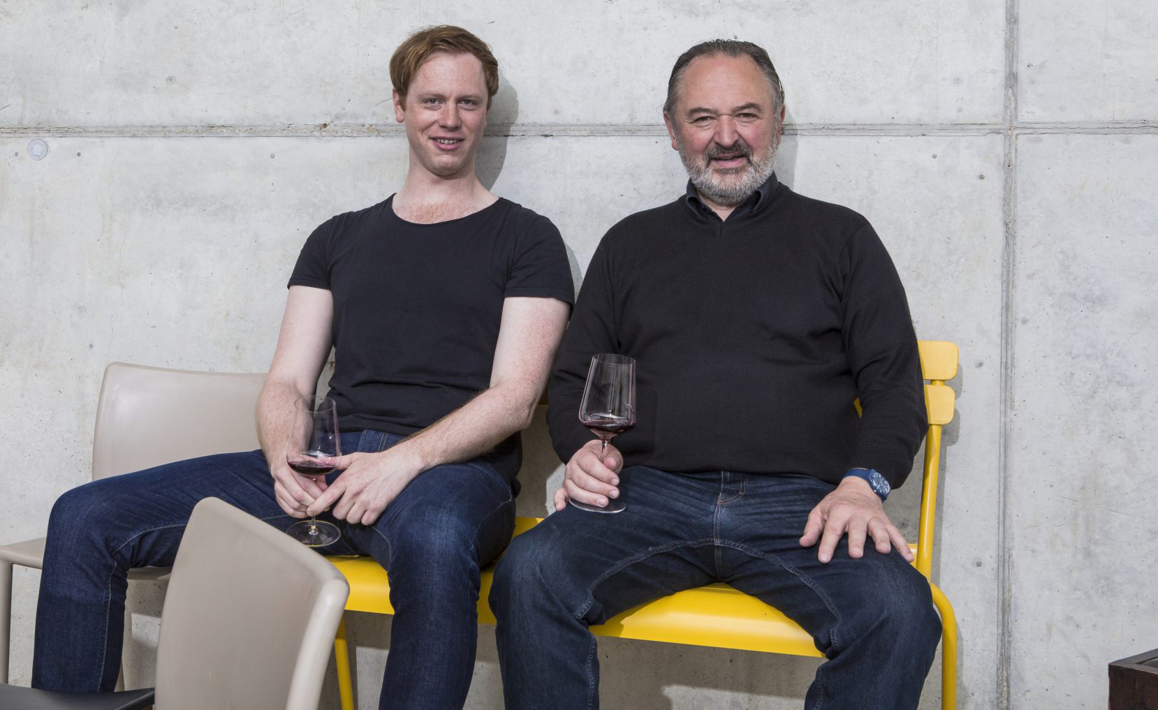 Hans und Martin Nittnaus sitzen auf Stühlen mit einem Glas Rotwein in der Hand