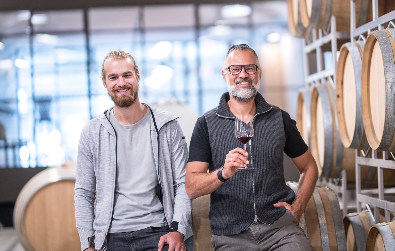 Clemens Strobl mit seinem Sohn, vor Weifässern mit Glas in der Hand